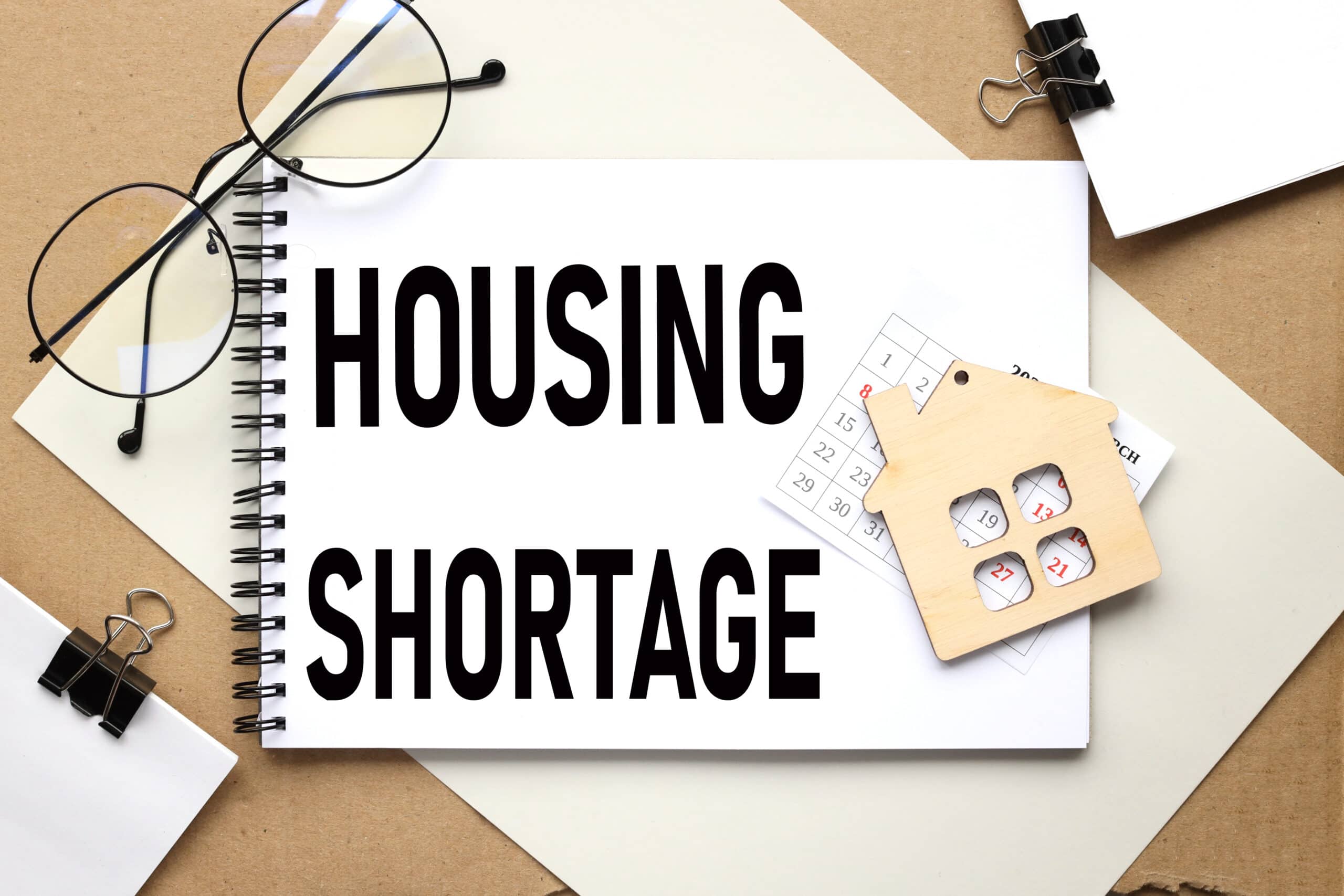 HOUSING SHORTAGE. the text on the notebook on which the wooden figure of the house lies Housing shortage